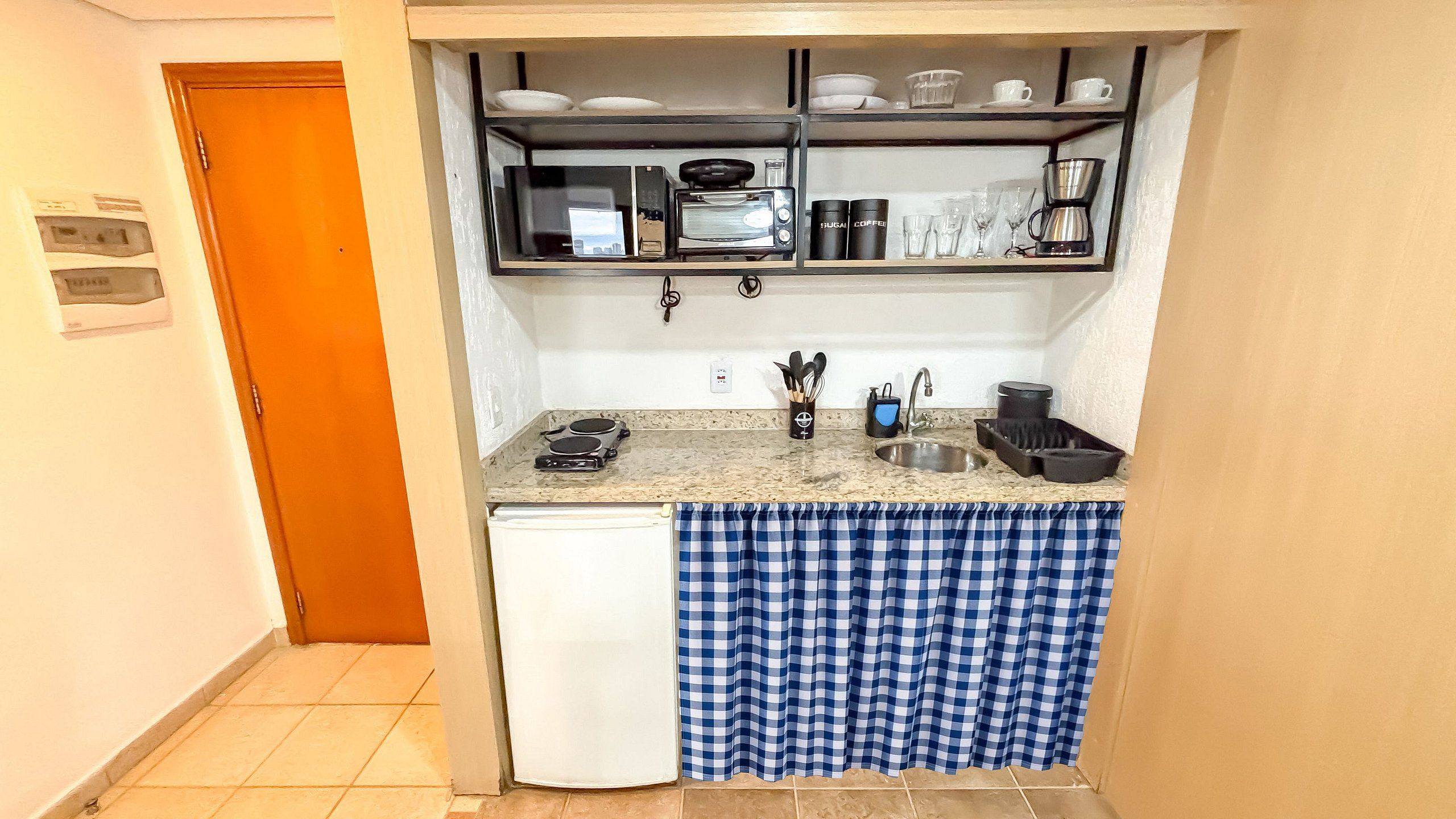 A compact kitchen with a refrigerator, coffee maker, and utensils on the counter.