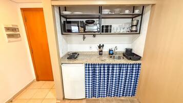 A compact kitchen with a refrigerator, coffee maker, and utensils on the counter.
