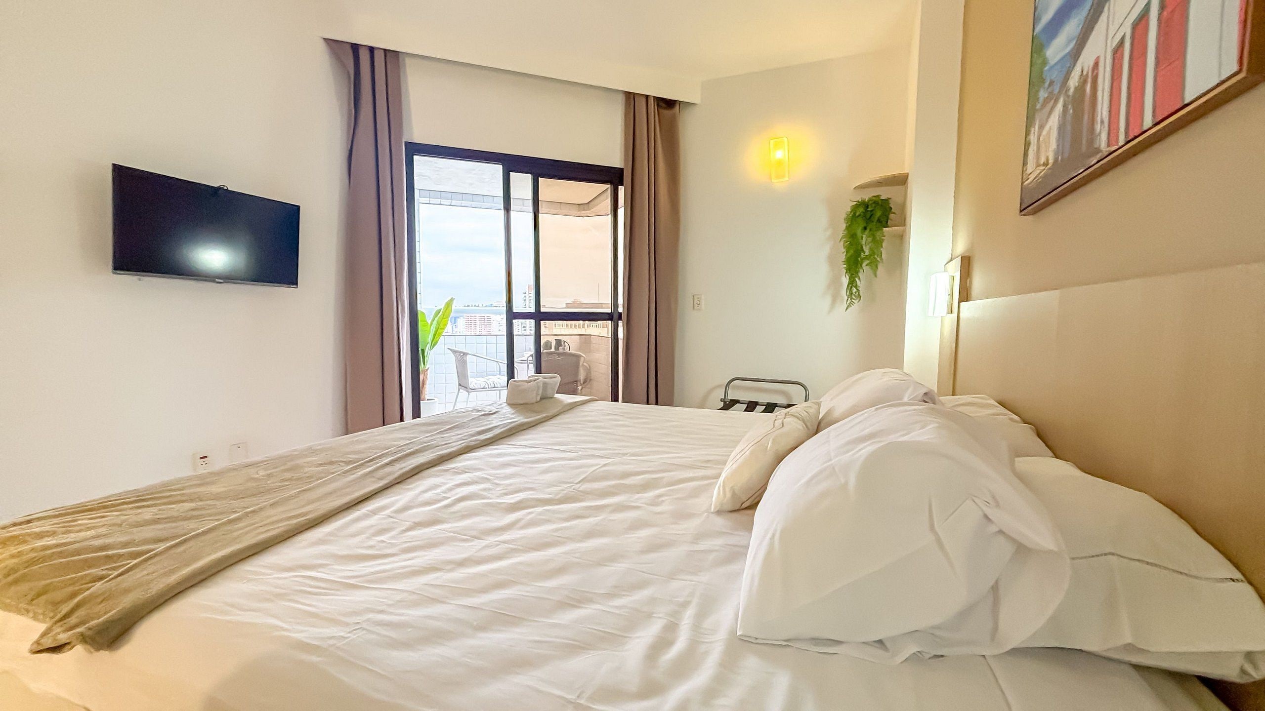 Une chambre d’hôtel avec un lit, un téléviseur fixé au mur, une fenêtre avec des rideaux et une vue sur la ville.