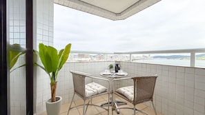 A balcony with a table and chairs, a potted plant, and a cityscape view. - SA - Clube XV - Apto CXV2103 (Santos)