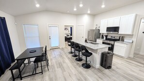 A modern kitchen with a central island, bar stools, and built-in appliances. - Modern Navy & Black 4BR Near Texas Tech (Lubbock)