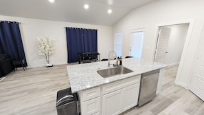 A modern kitchen with a granite countertop, stainless steel sink, and white cabinetry. - Modern Navy & Black 4BR Near Texas Tech (Lubbock)