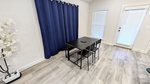 A room with a table and chairs, a blue curtain, a white wall, and a door with blinds. - Modern Navy & Black 4BR Near Texas Tech (Lubbock)
