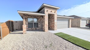 A residential property with a brick exterior, a garage, and a gravel driveway. - Modern Navy & Black 4BR Near Texas Tech (Lubbock)