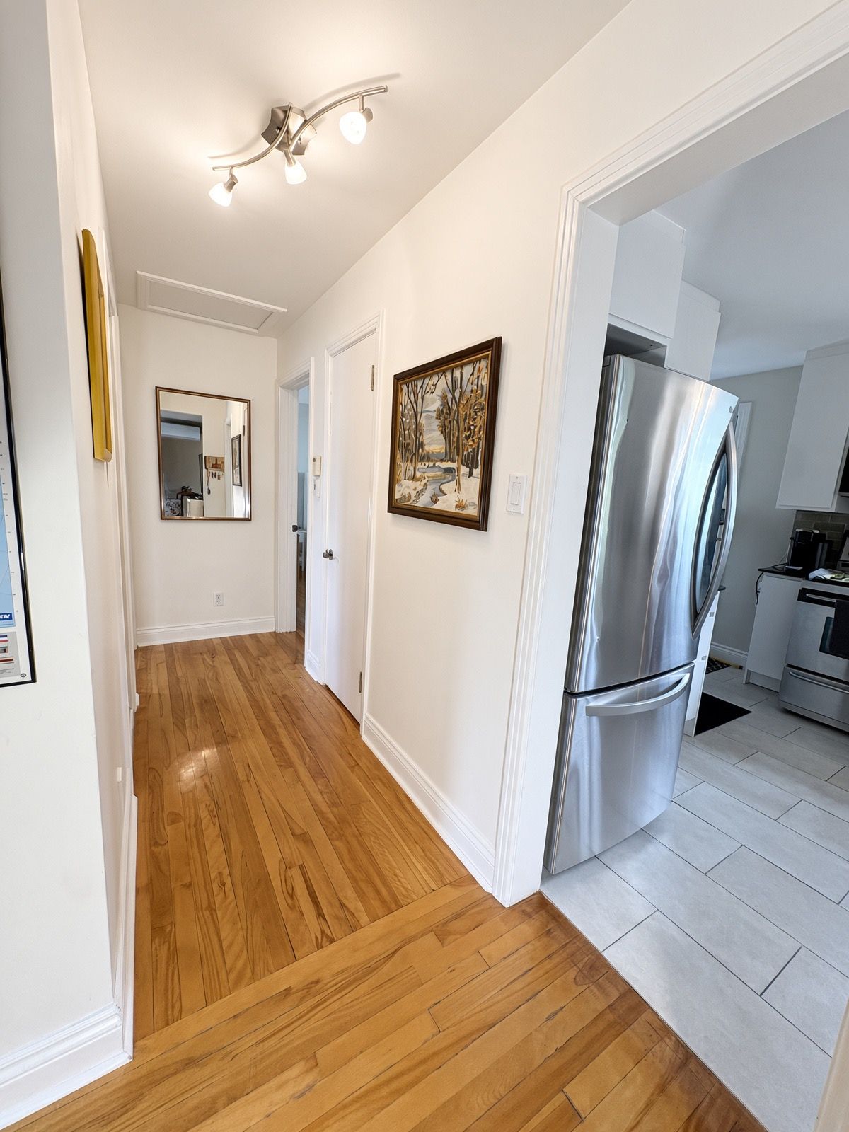 A kitchen with a stainless steel refrigerator, a wooden floor, and a painting on the wall.