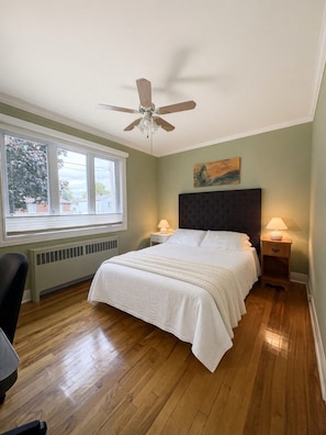 Une chambre à coucher avec un lit, un ventilateur de plafond, une fenêtre et un radiateur.