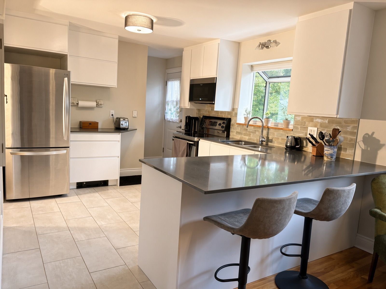 A modern kitchen with a stainless steel refrigerator, a built-in oven, and a large island with bar stools.