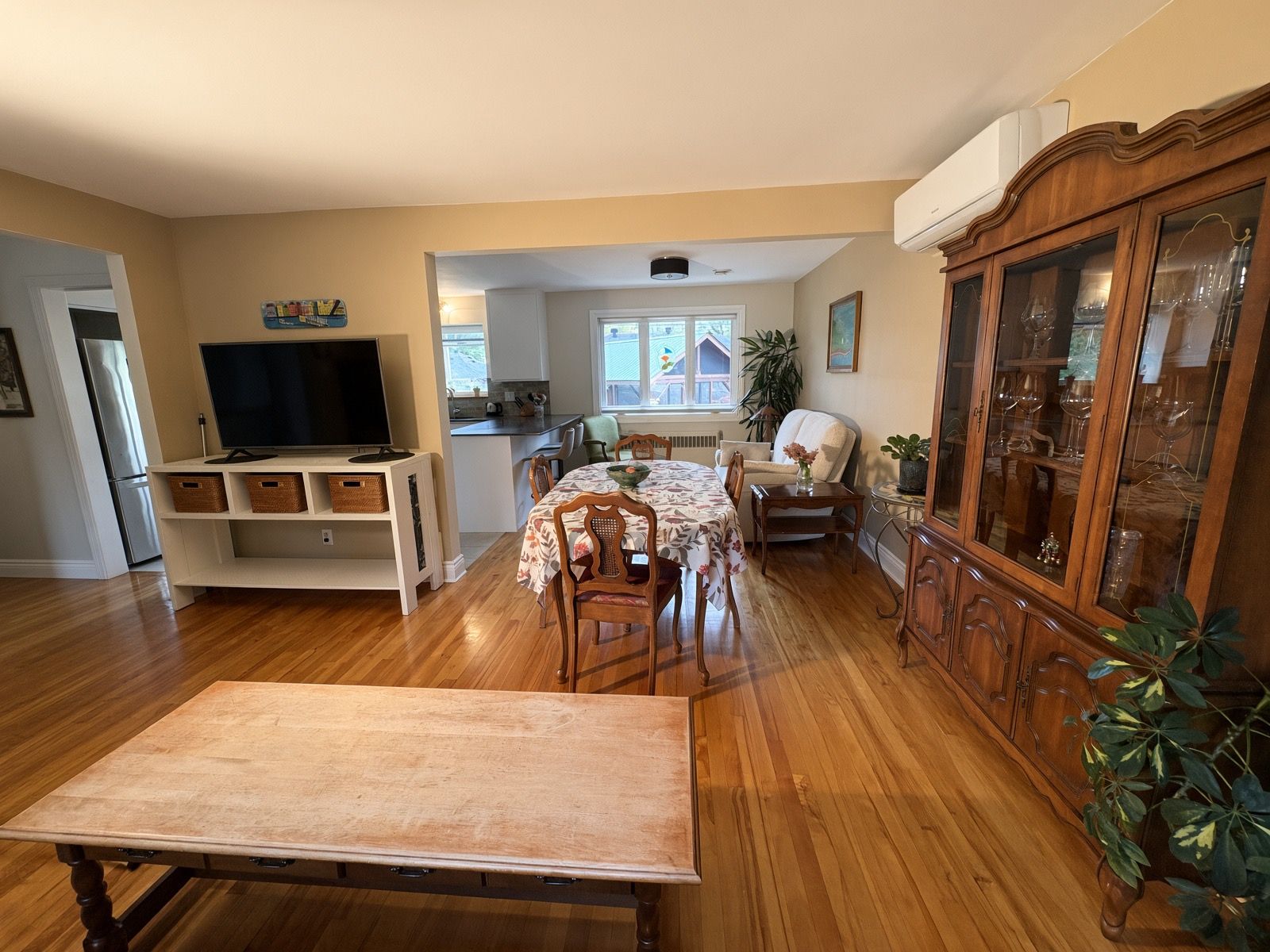 Una sala de estar amplia con comedor, televisor y un mueble con puertas de cristal.