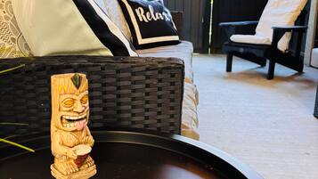 Sofá de vime com almofada 'Relax', mesa de bandeja trançada e uma estátua tiki.