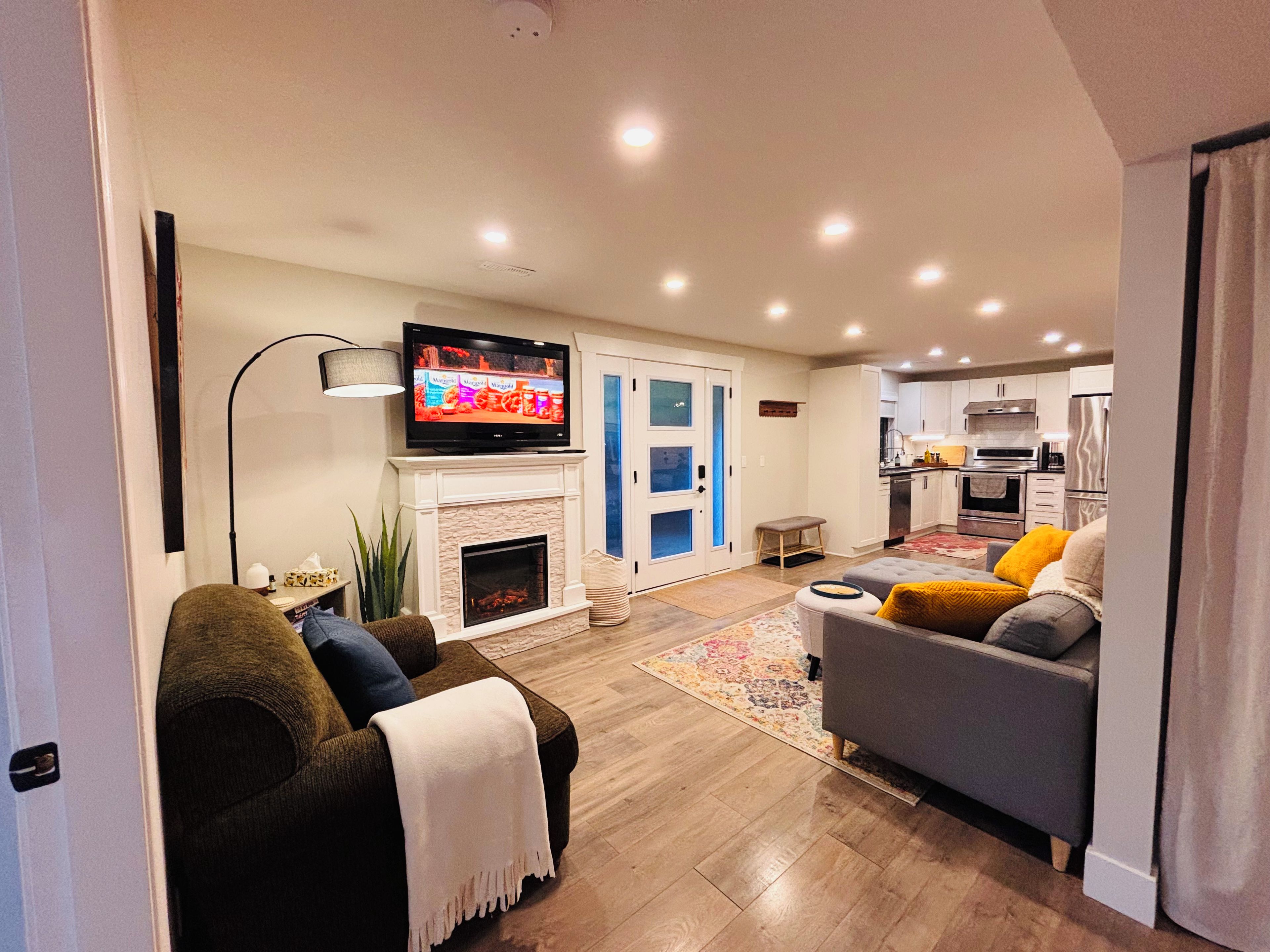 A modern living room with a fireplace, a television, and a kitchen in the background.