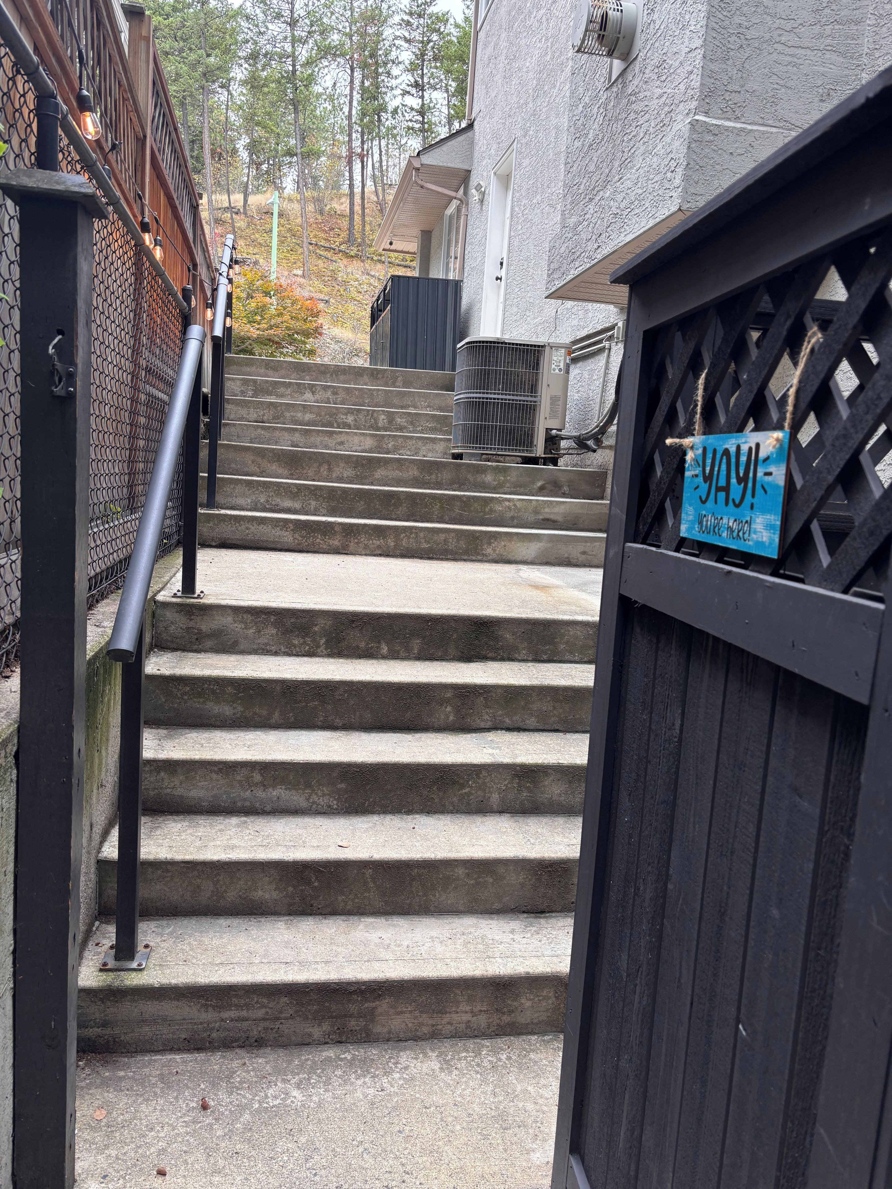 A set of concrete stairs leading to a building entrance, with a metal gate and a 'YAY! you're here!' sign.