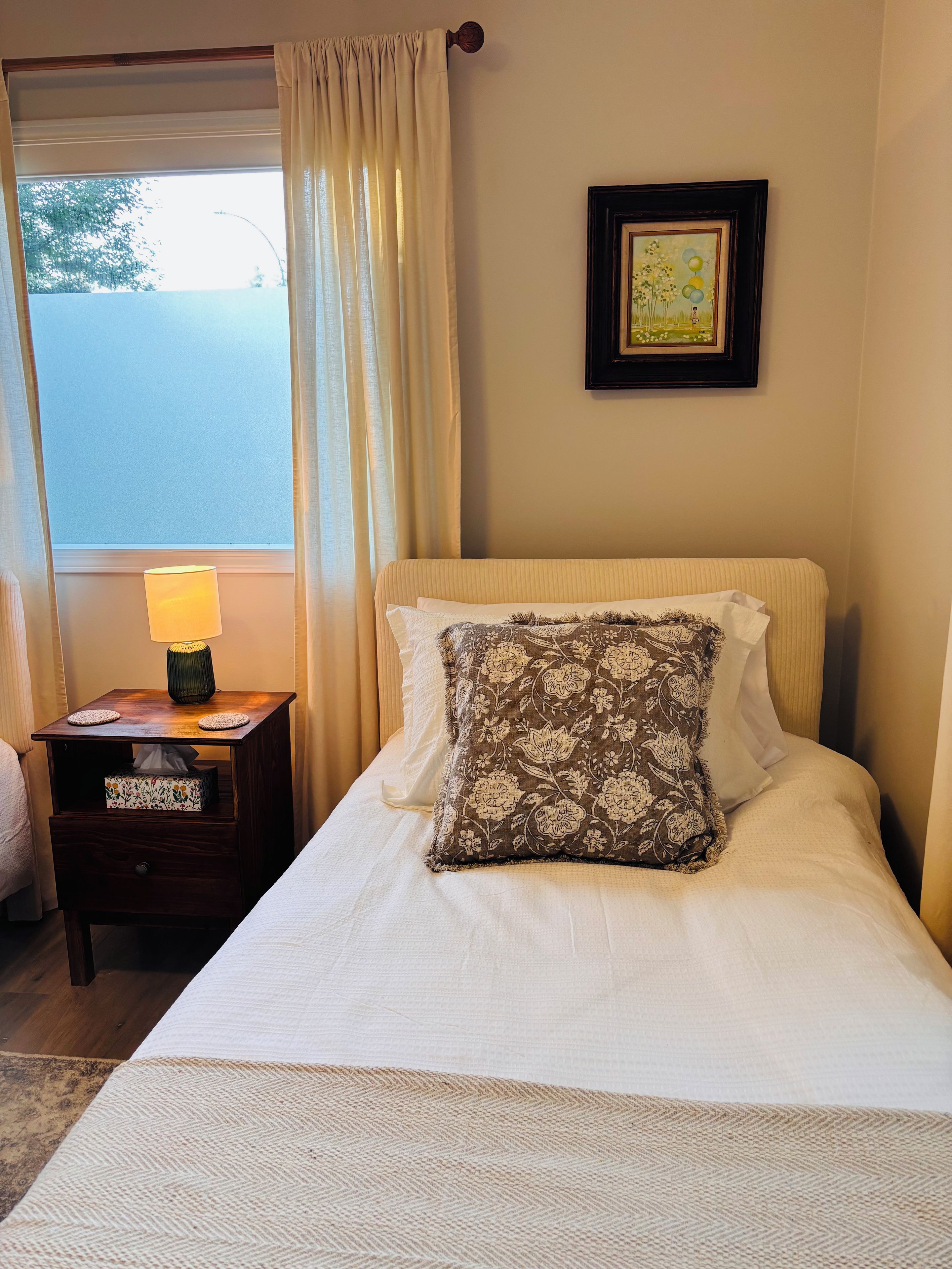 A neatly made bed with a floral pillow, a bedside lamp, and a framed picture on the wall.