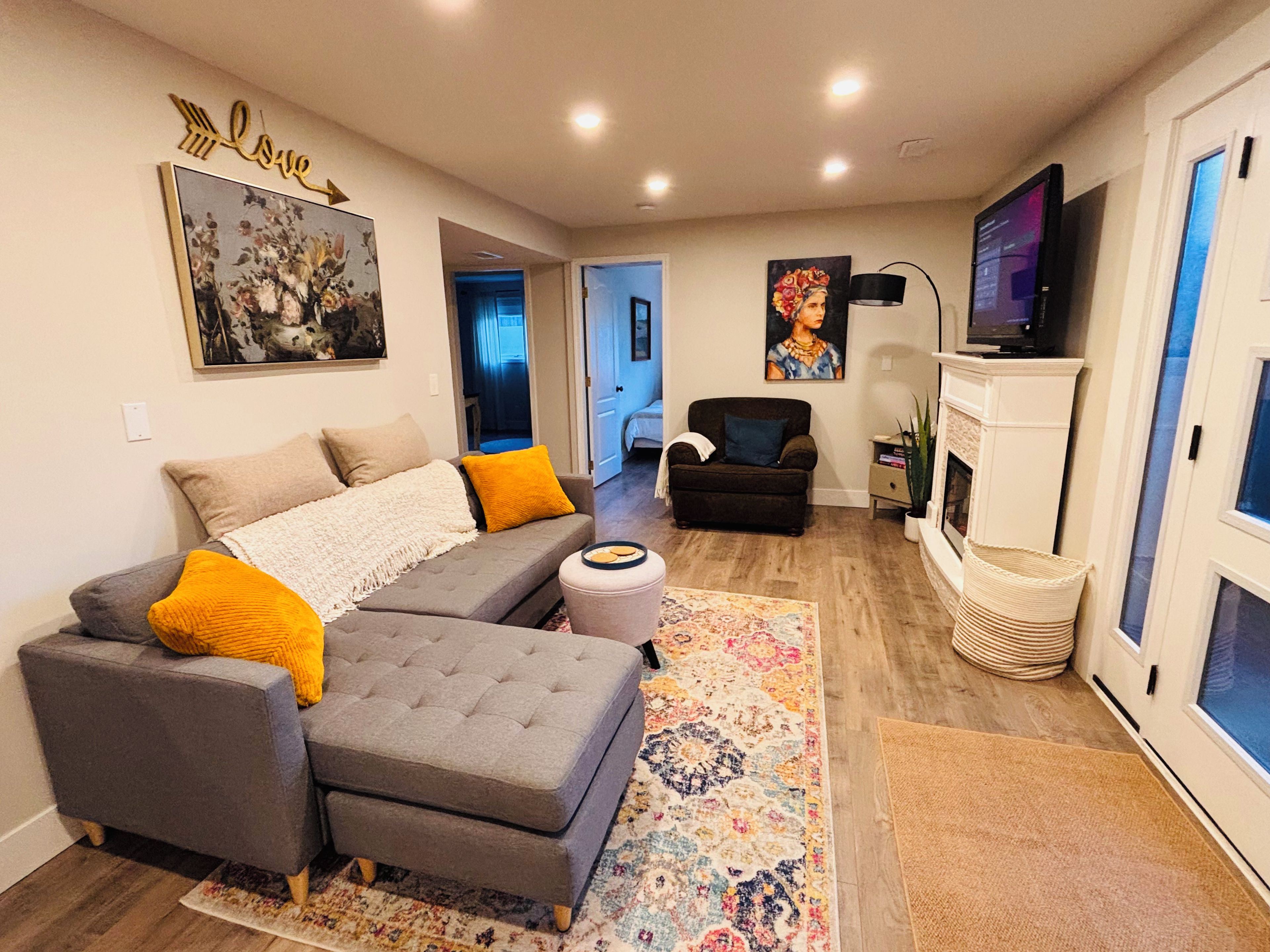 A living room with a sectional sofa, ottoman, and a flat-screen TV.