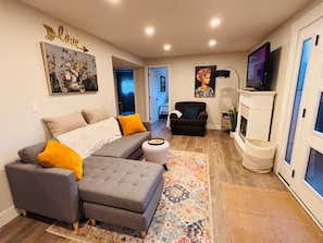 Ein Wohnzimmer mit Ecksofa, Hocker und Flachbildfernseher.