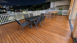 Una terraza de madera con una mesa y sillas, rodeada por una barandilla blanca.