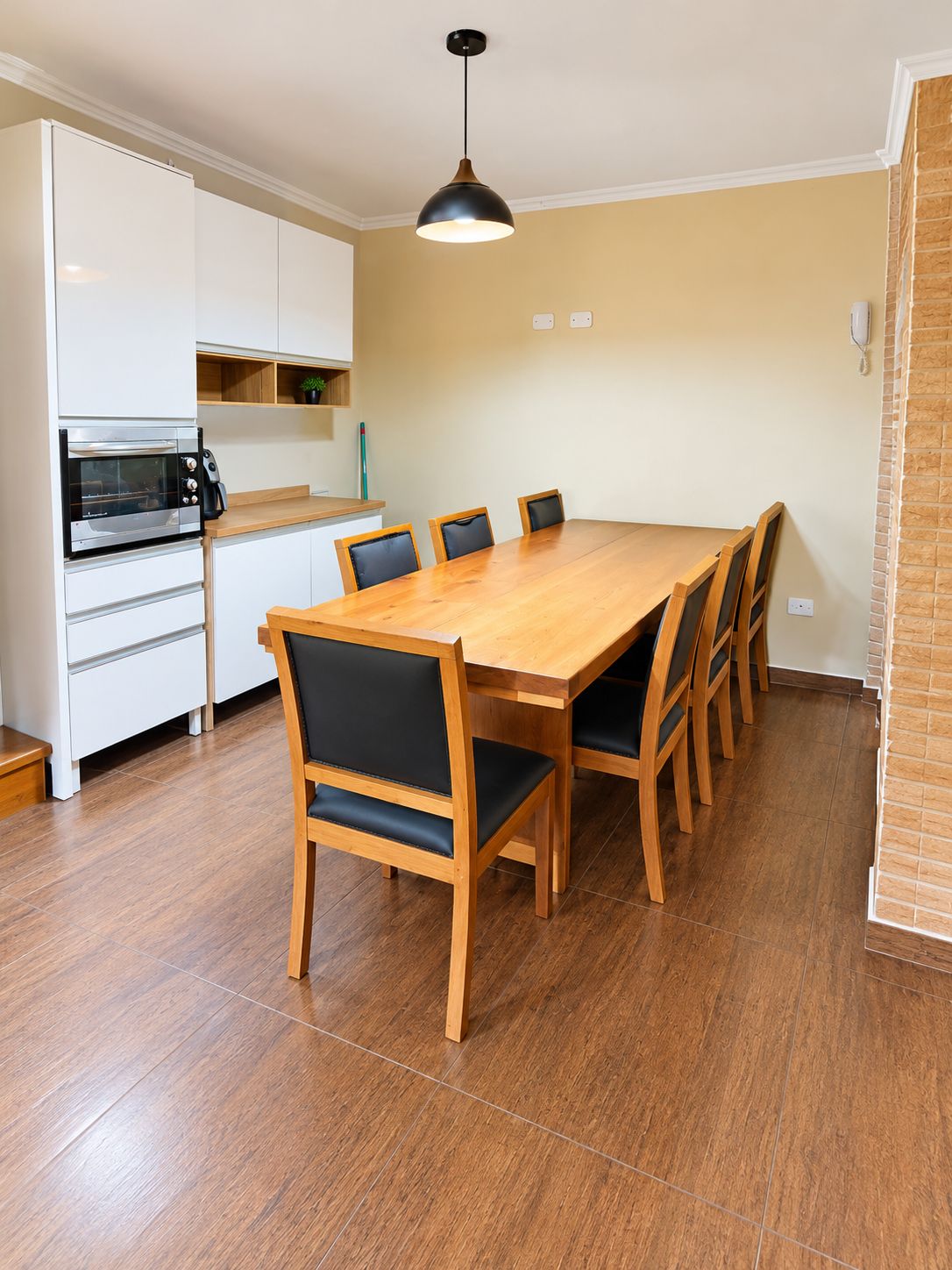 Un comedor con una mesa y sillas de madera, horno empotrado y lámpara colgante.