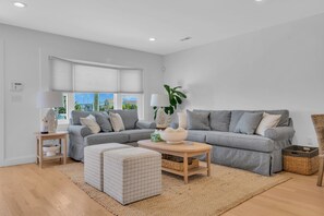 Un salon moderne avec un canapé d’angle gris, une table basse et un pouf à motifs.