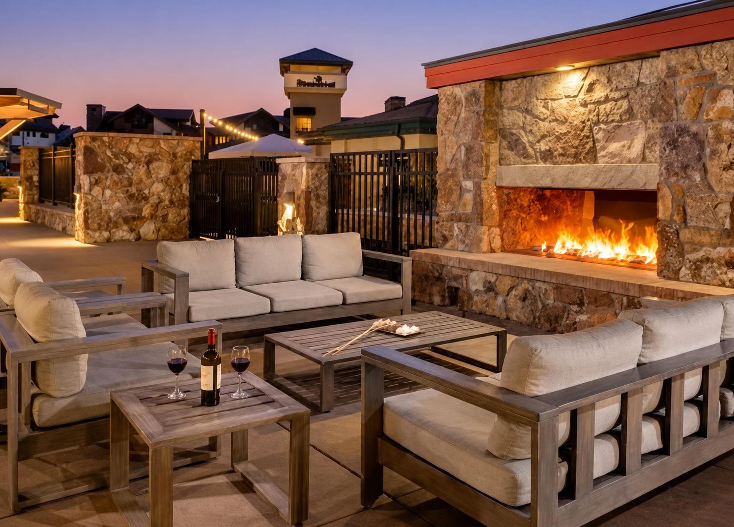 An outdoor seating area with stone walls, a fire feature, and a view of the surrounding buildings.