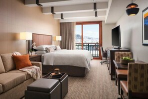 A hotel room with a bed, a sofa, a desk, a television, and a balcony with a view of snow-covered mountains. - Ski in Ski out Resort at base of Steamboat Springs (Steamboat Springs)