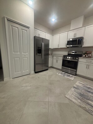 A kitchen with white cabinets, a stainless steel refrigerator, a microwave, an oven, and a tiled floor. -     Beautiful 3-Bedroom Villa with Lake & Golf Course Views (Punta Gorda)