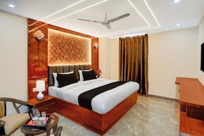 Una habitación de hotel con cama, escritorio, silla, ventilador de techo y televisor.