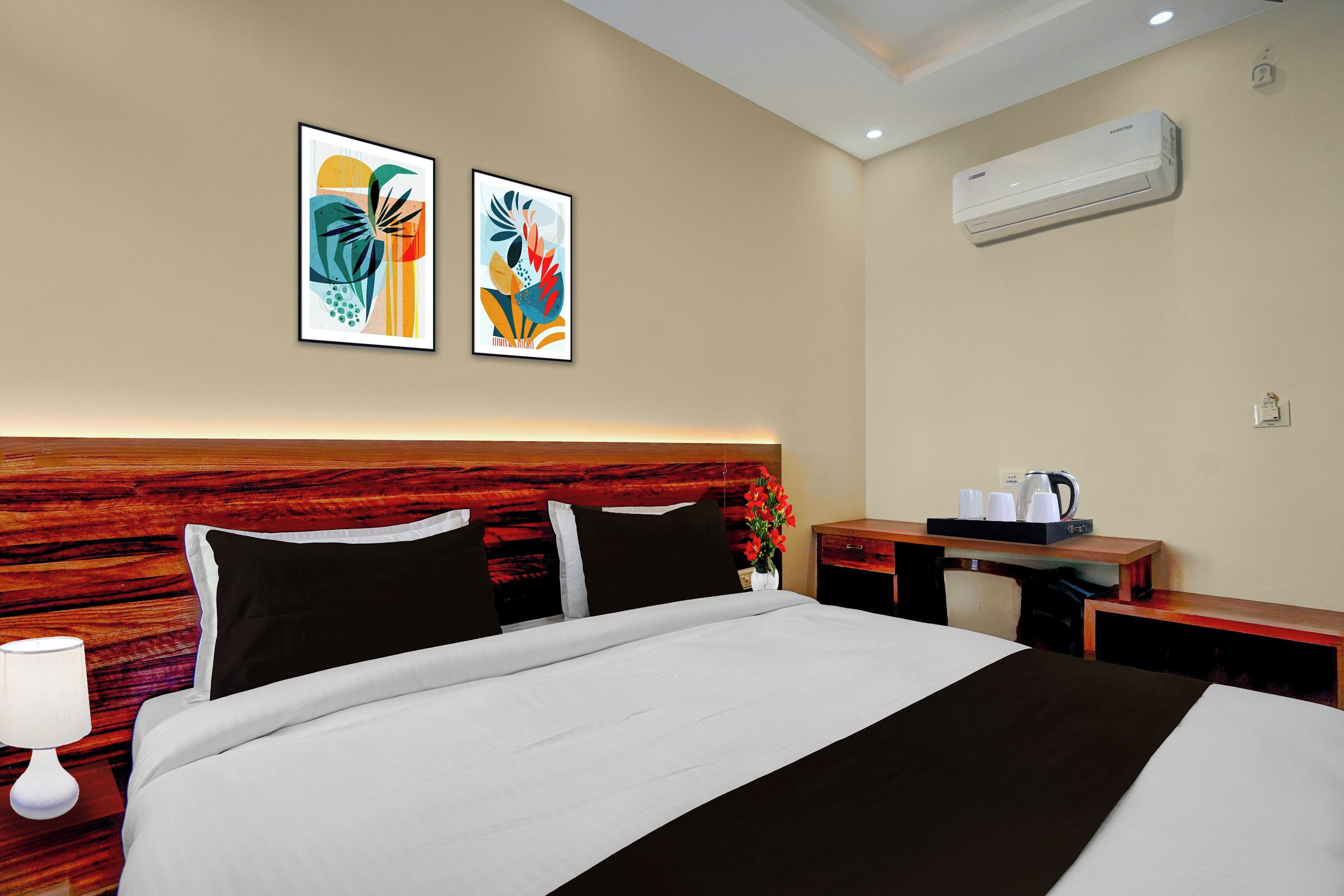 Habitación de hotel con cama, mesita de noche, escritorio, aire acondicionado de pared y dos cuadros abstractos.