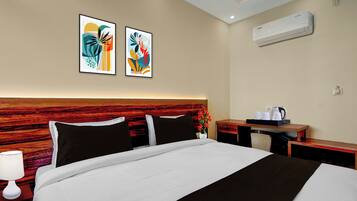 Habitación de hotel con cama, mesita de noche, escritorio, aire acondicionado de pared y dos cuadros abstractos.