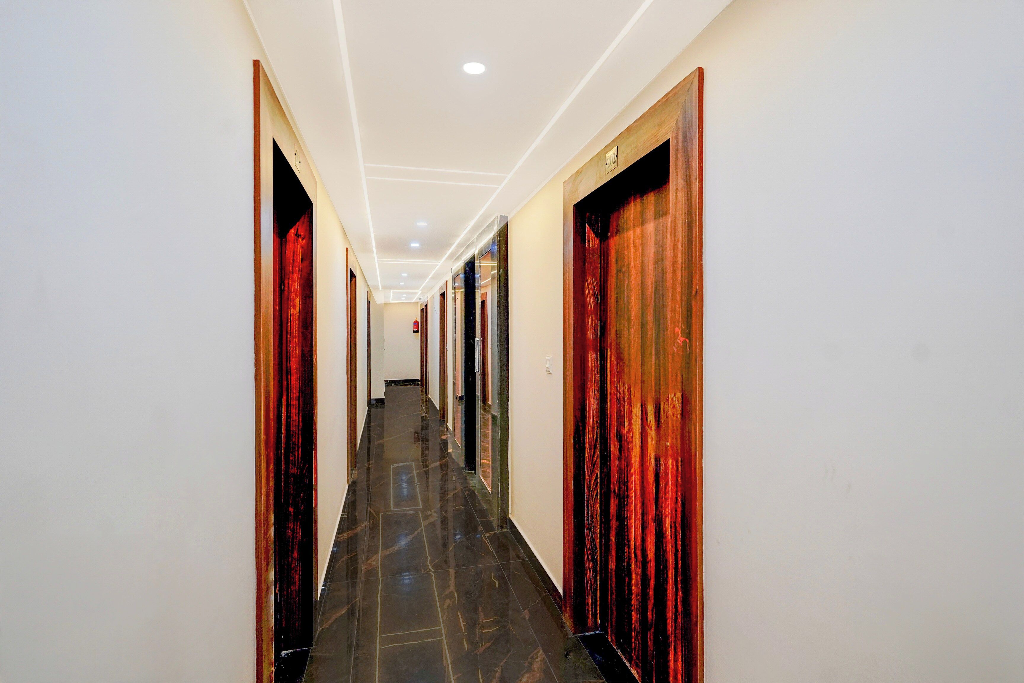 A hotel hallway with doors on both sides, a tiled floor, and recessed lighting.