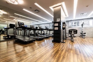 A gym with treadmills, weight machines, and a wooden floor. - Affordable Suite | Steps to Subway & Parks (Toronto)