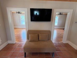A living room with a beige sofa, a flat-screen TV mounted on the wall, and a wooden floor. - Cowboy Casita~Walk to 11th St. Cowboy Bar (Bandera)