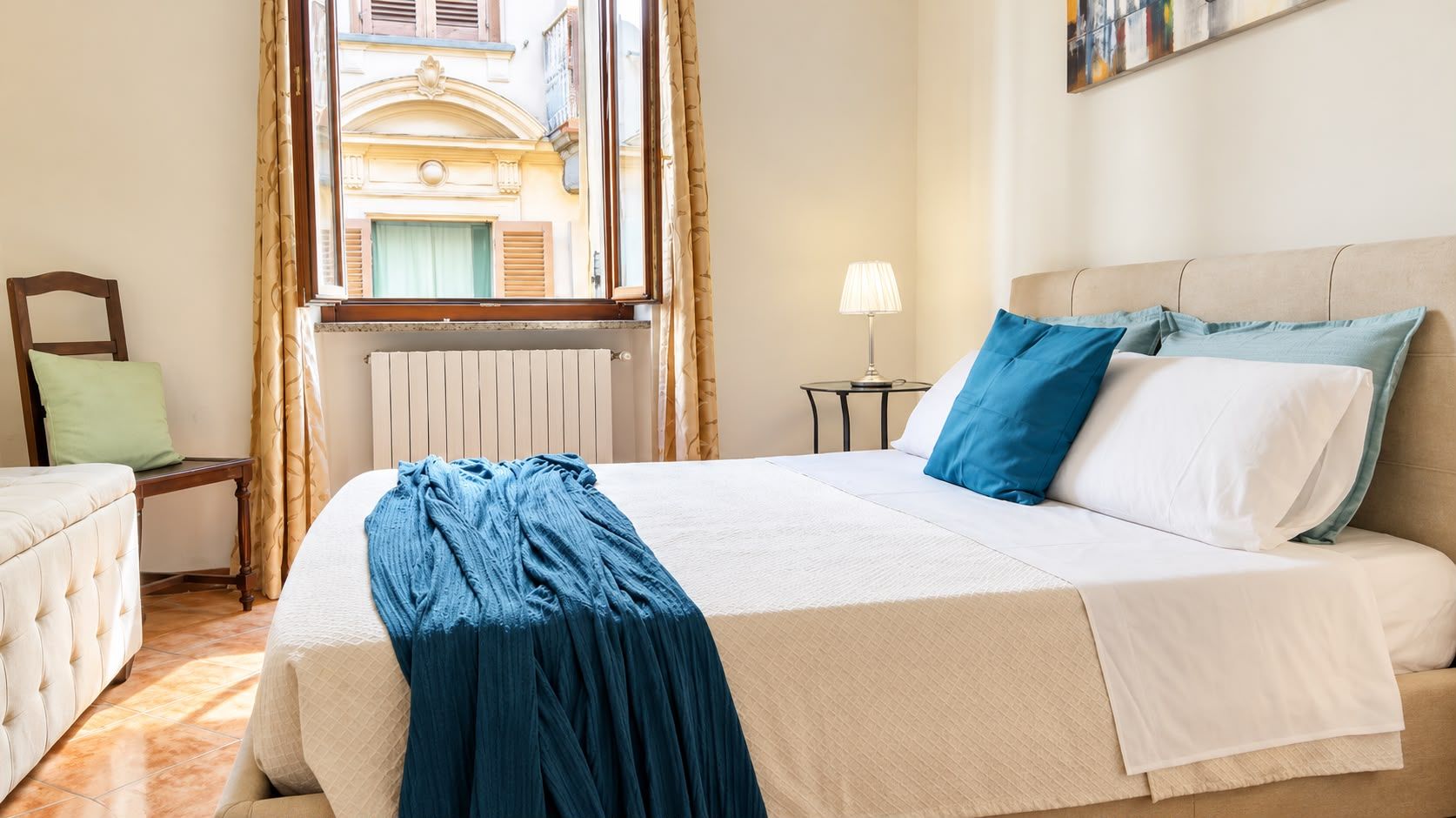 A hotel room with a bed, a chair, a table, and a window with curtains.