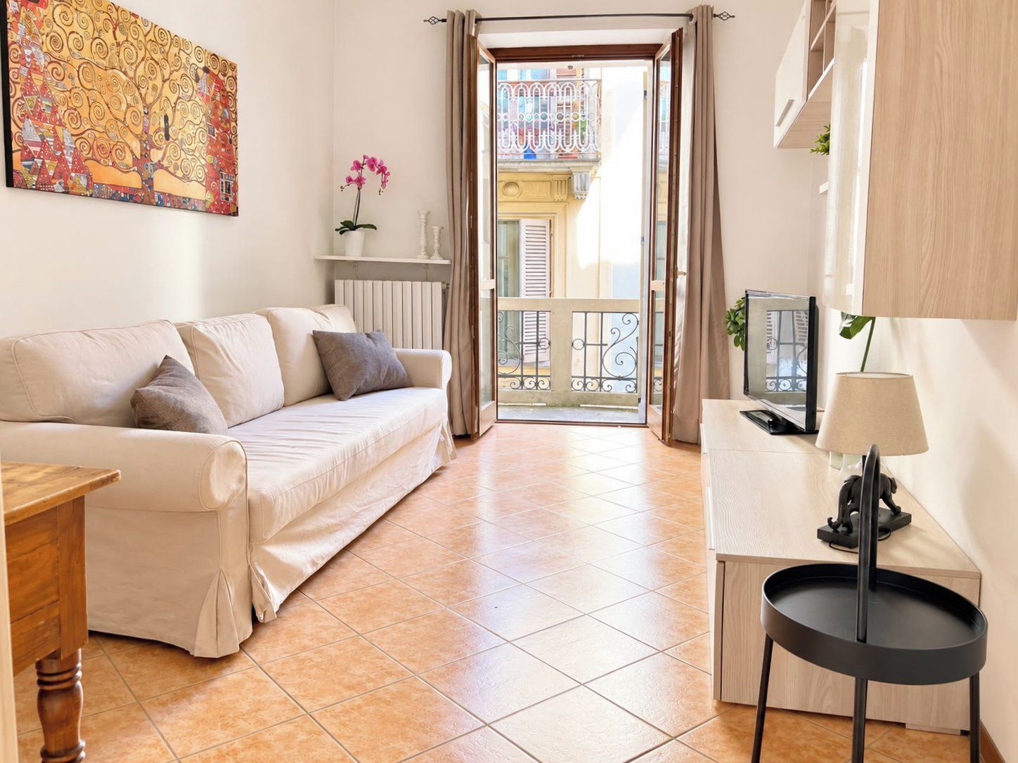 Un salon moderne avec un canapé, une petite table, une lampe et une vue sur un balcon doté d’une balustrade.