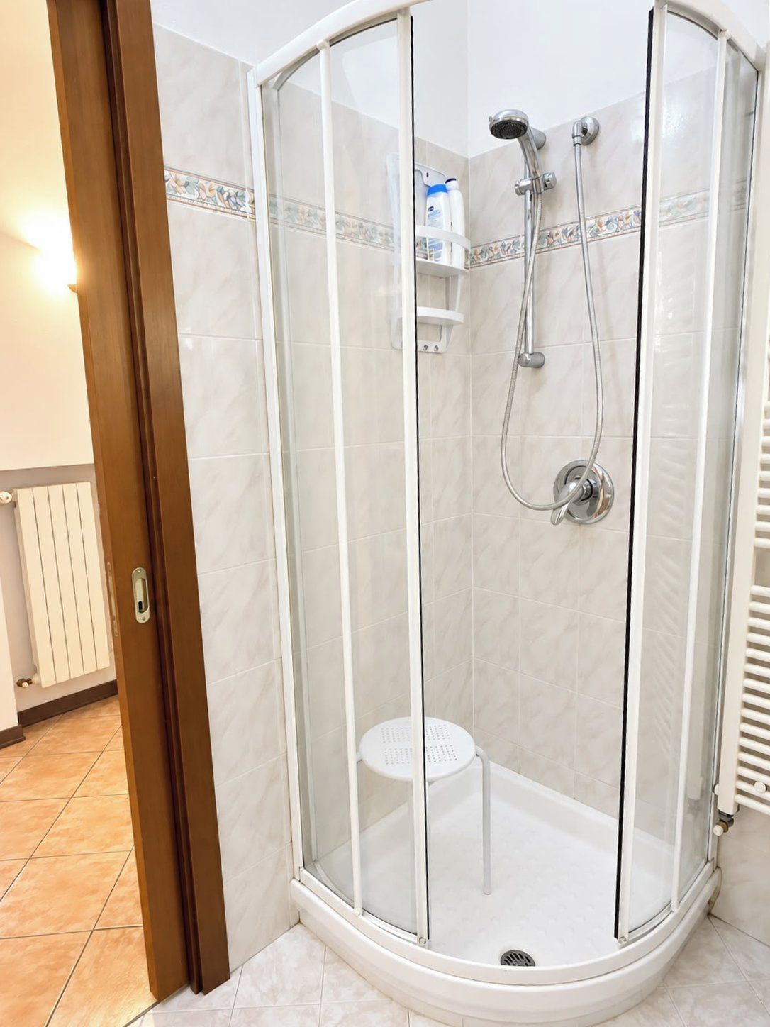 A glass-enclosed shower stall with a white tiled floor and a white toilet in the corner.