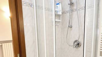 A glass-enclosed shower stall with a white tiled floor and a white toilet in the corner.