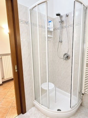 A glass-enclosed shower stall with a white tiled floor and a white toilet in the corner. - QuickHome Via Italia 43 (Biella)