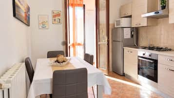 Een functionele keuken met een eettafel, stoelen, een koelkast, een magnetron en een oven.