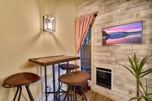 A room with a wooden wall, a table with stools, a mounted TV, and a window with curtains. - Updated North Tahoe Studio | Pool, Spa & Pines (Tahoe Vista)