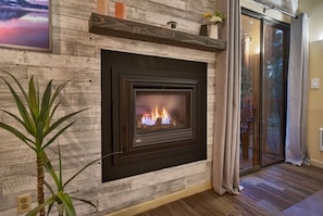 Ein Kamin mit modernem Design, eine Holzwand und eine Pflanze daneben.