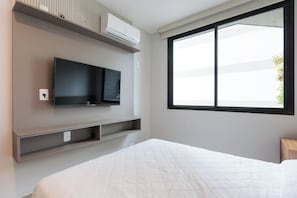 Een moderne slaapkamer met een bed, een wandtelevisie, een raam en inbouwkasten.