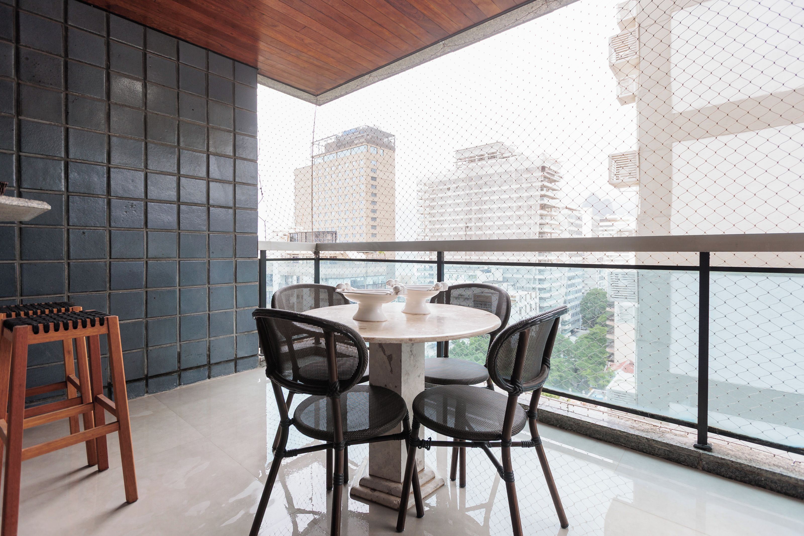 Un balcon avec une table ronde et des chaises, un tabouret en bois, et une vue sur les bâtiments de la ville.