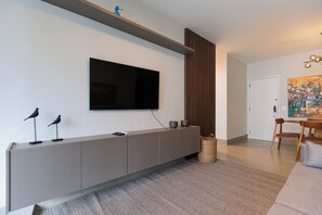 A modern living room with a flat-screen TV mounted on a wall, a grey console table with decorative items, and a woven basket on the floor. - New Listing (Rio de Janeiro)