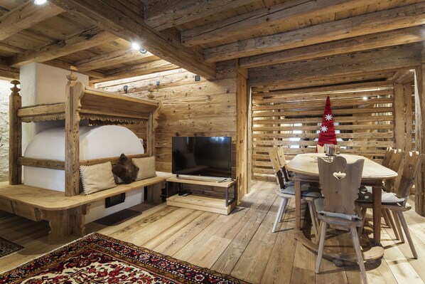 Un interior rústico con techo de madera, chimenea, televisor y comedor con mobiliario de madera.