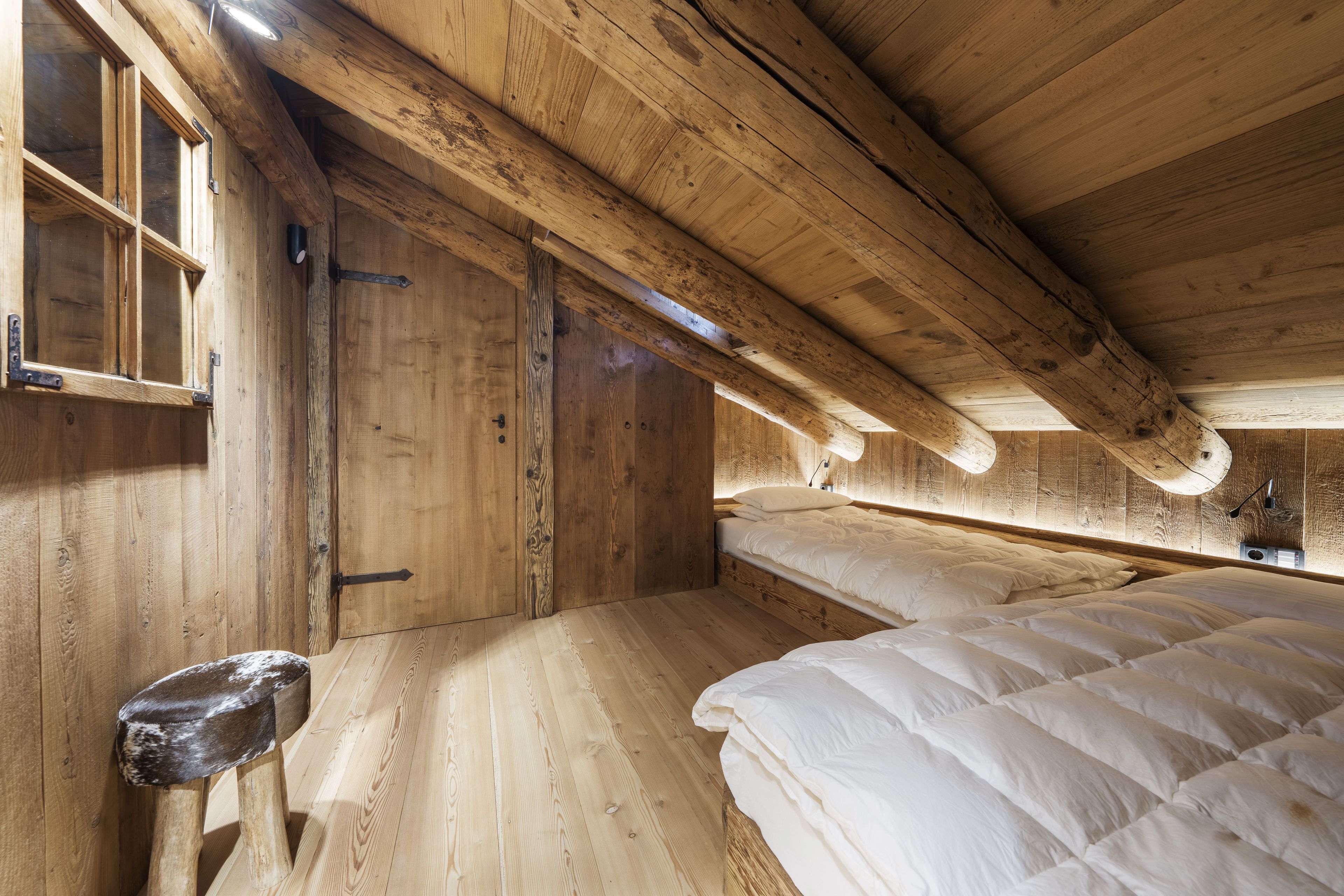 Un interno in legno con un letto, una panca e una porta.