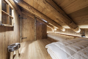 Un interno in legno con un letto, una panca e una porta.