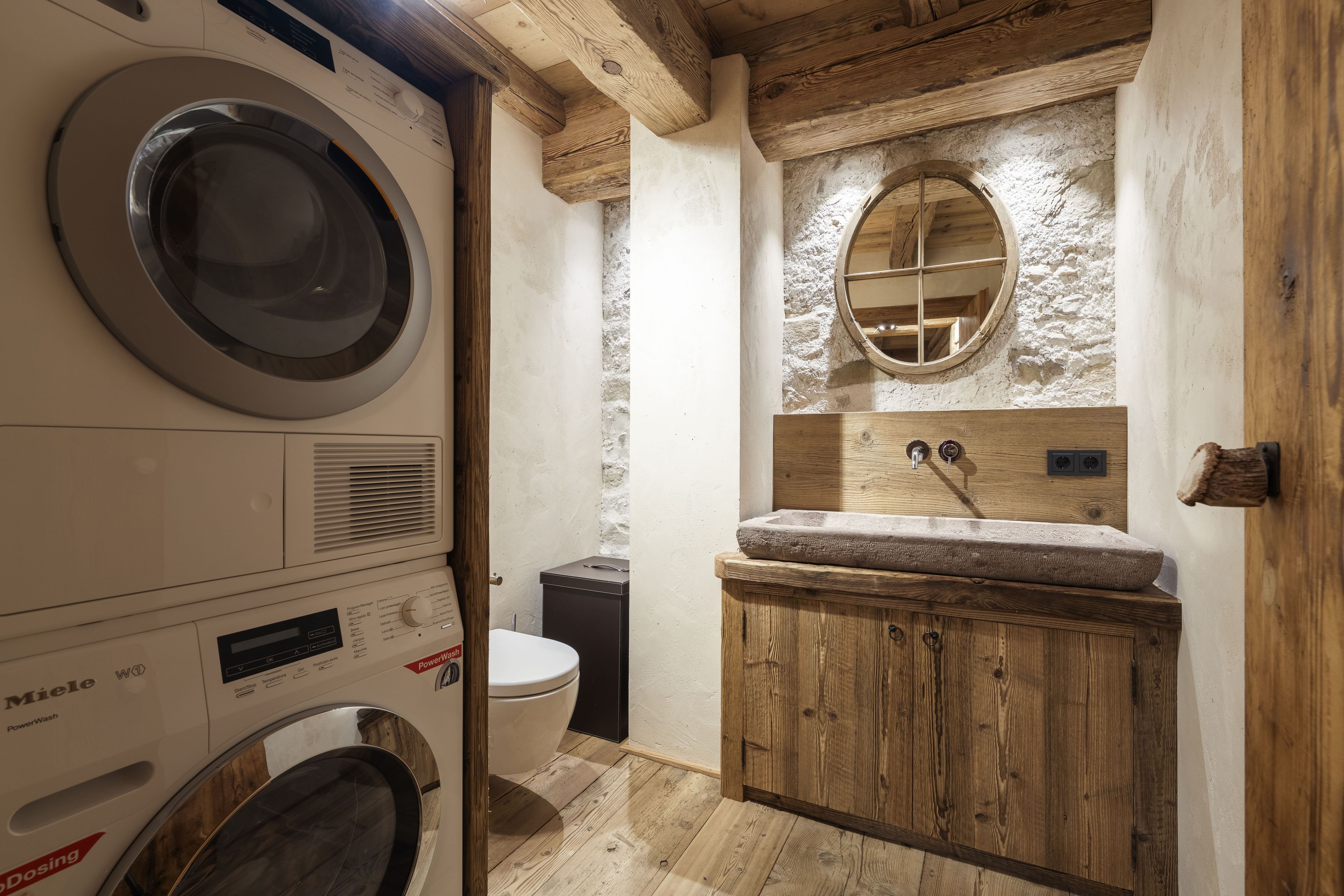 Una lavanderia funzionale con lavatrice, water e lavabo con mobiletto in legno.