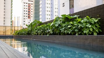 Una piscina con borde de azulejos, rodeada por un muro de ladrillo bajo y exuberante vegetación.