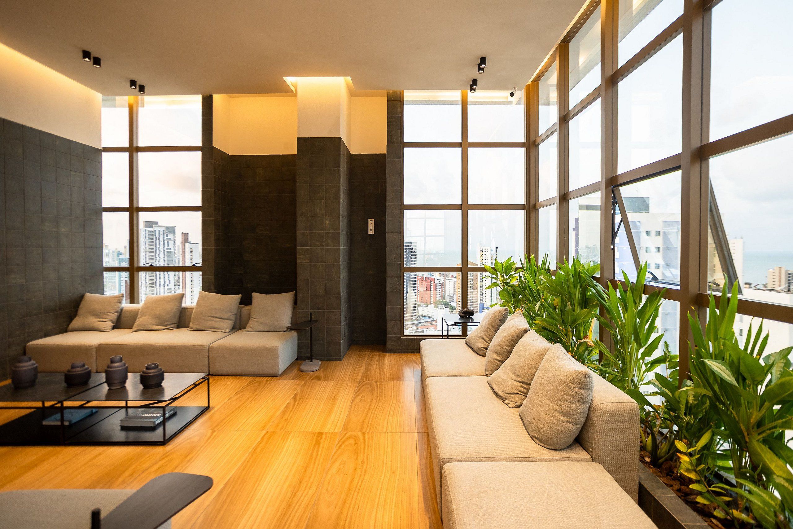 Una sala de estar moderna con un conjunto de sofás, una mesa de centro y vistas a un paisaje urbano a través de amplias ventanas.