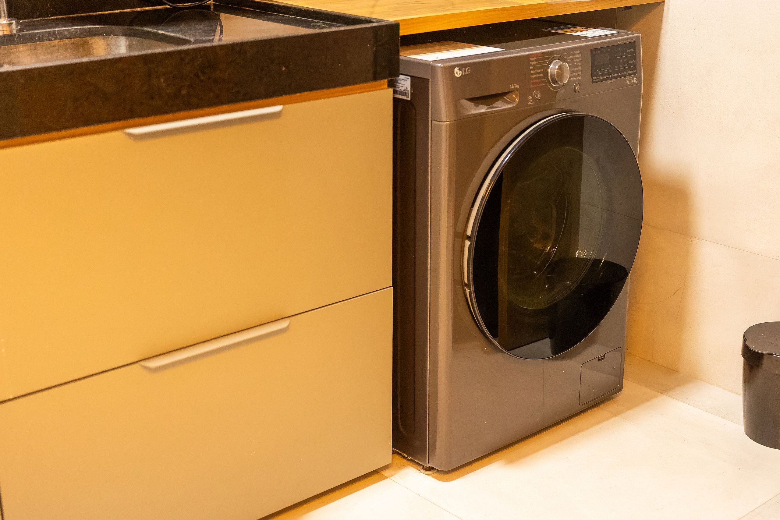 Cocina compacta y moderna con lavadora integrada, encimera y cubo de basura.