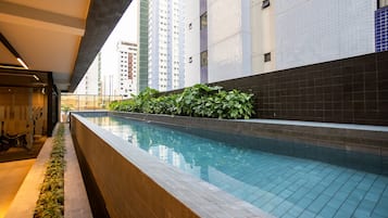 Una piscina con borde de azulejos, rodeada por un muro bajo y vegetación.