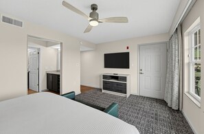 A hotel room with a bed, a ceiling fan, a television, a small cabinet, and a window with curtains. - Pigeon Forge Condo with Balcony | Newly Renovated! (Pigeon Forge)